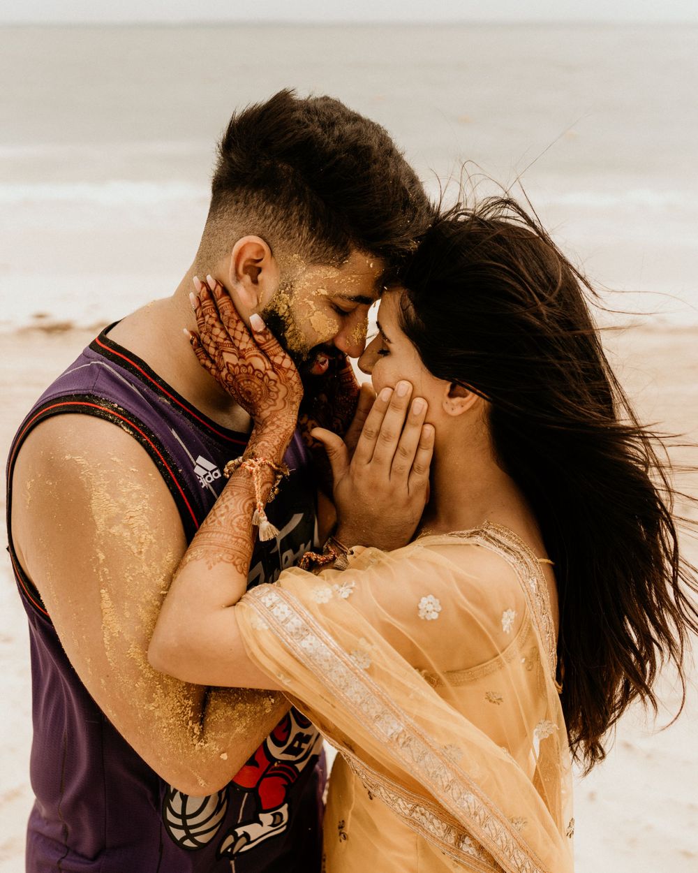 A romantic moment between a couple on a beach with henna tattoos and traditional attire.