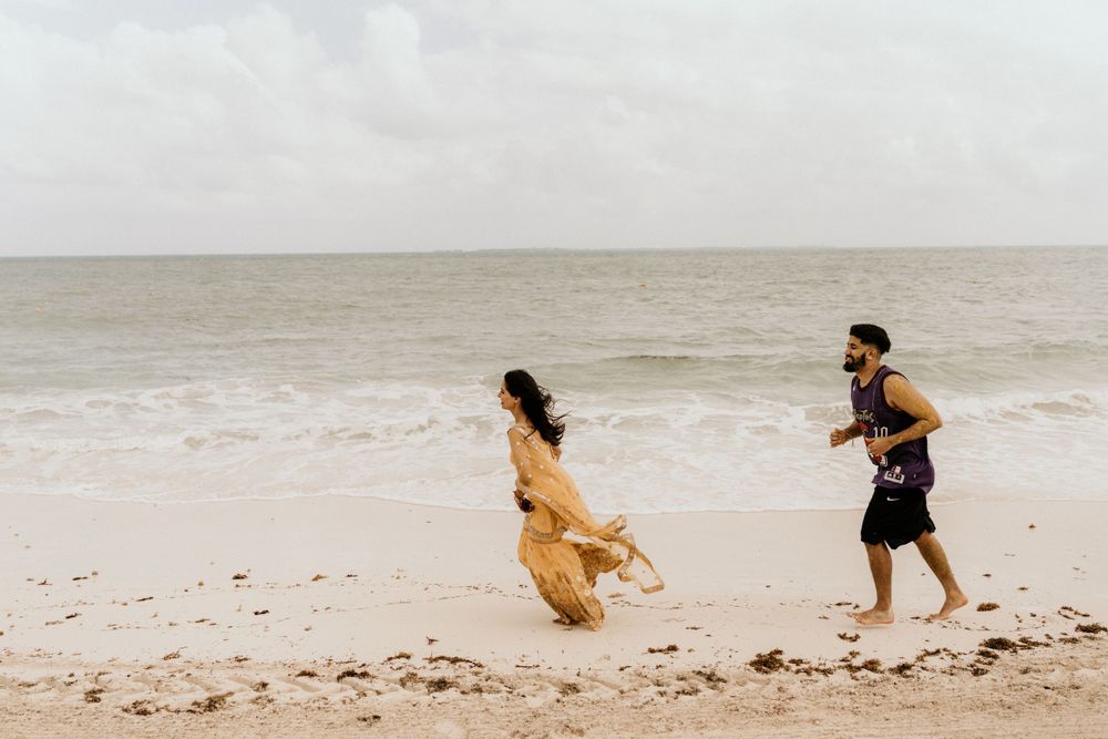 Two people running playfully along a misty beach shore with waves in the background.