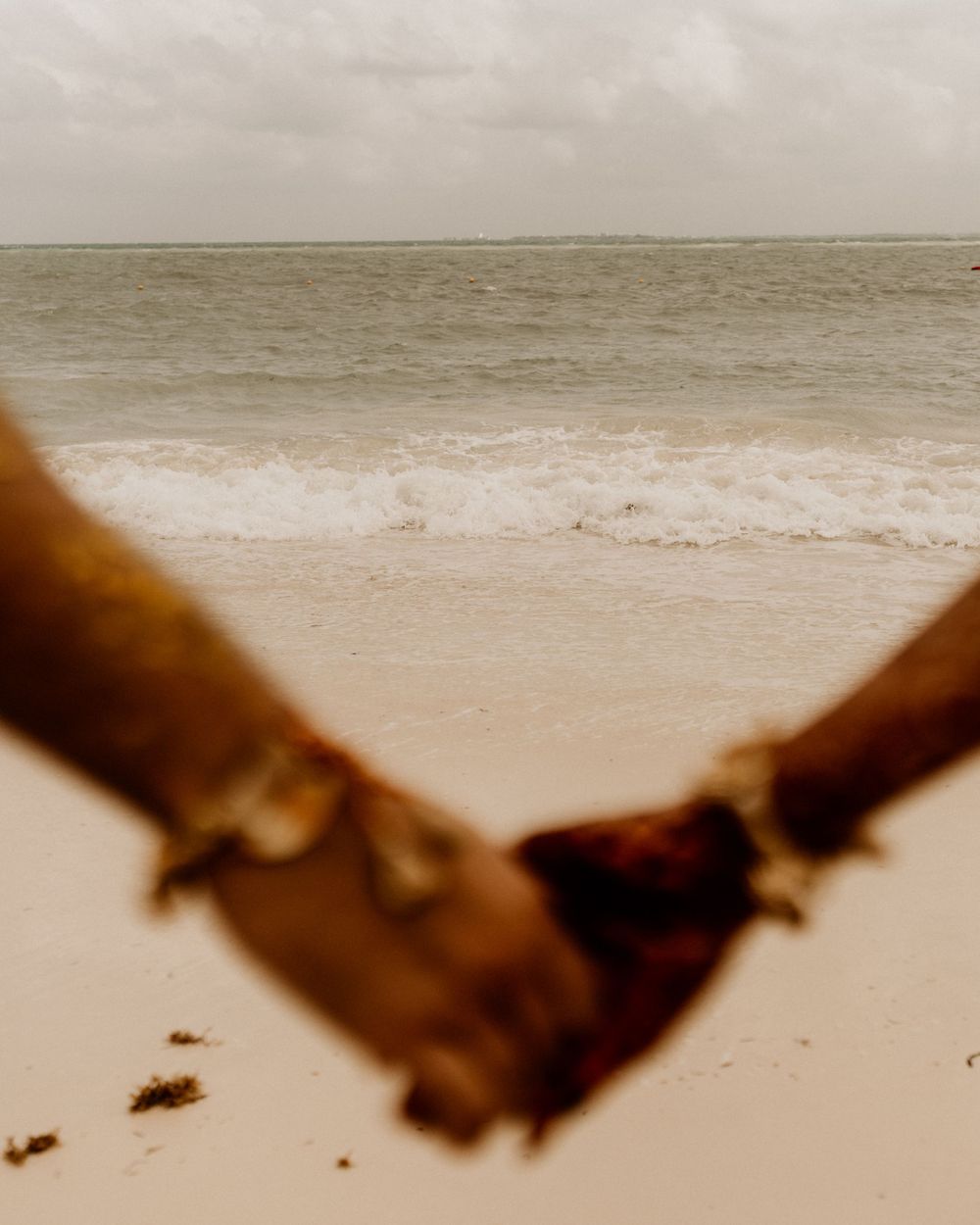 Close-up view of two hands clasped together against a serene beige beach backdrop.