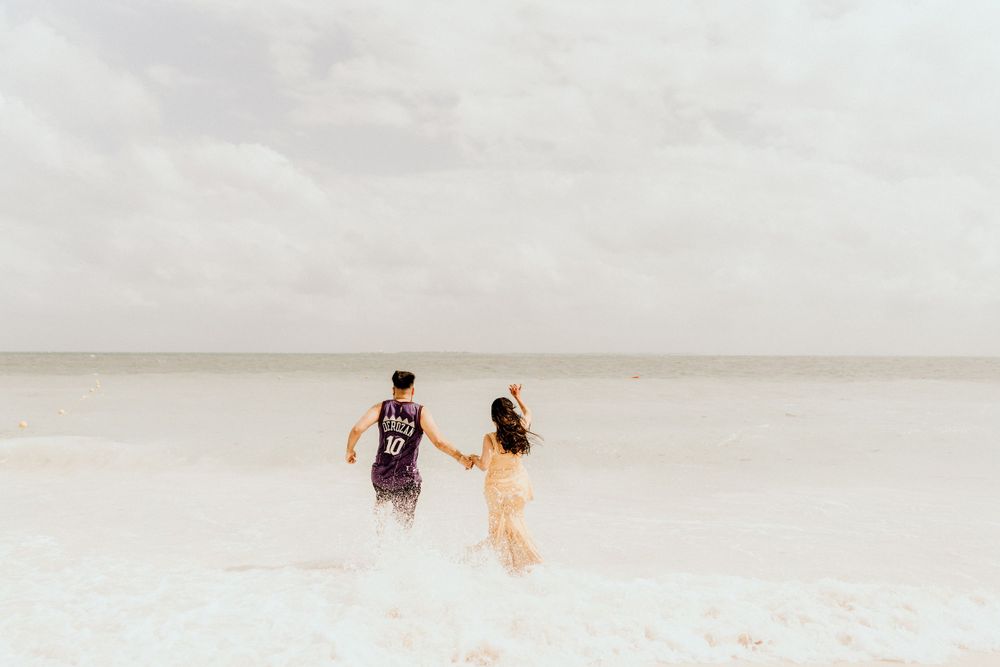 Two people walk together on a vast empty white beach under an overcast sky.