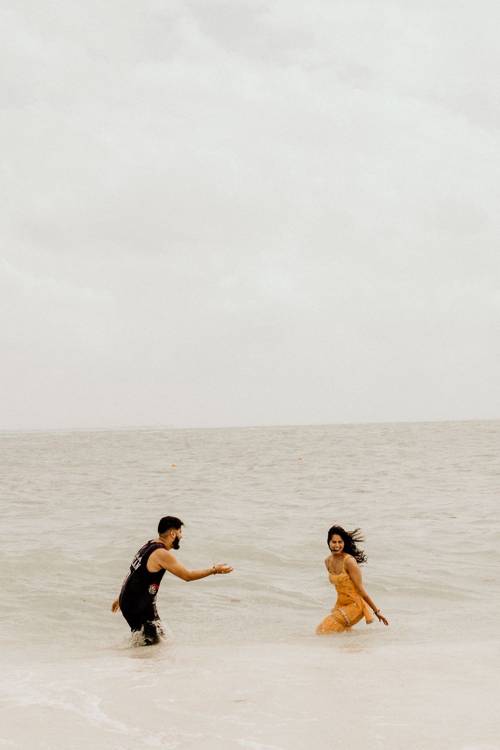 Two people playing and running through shallow ocean waves on a misty beach.