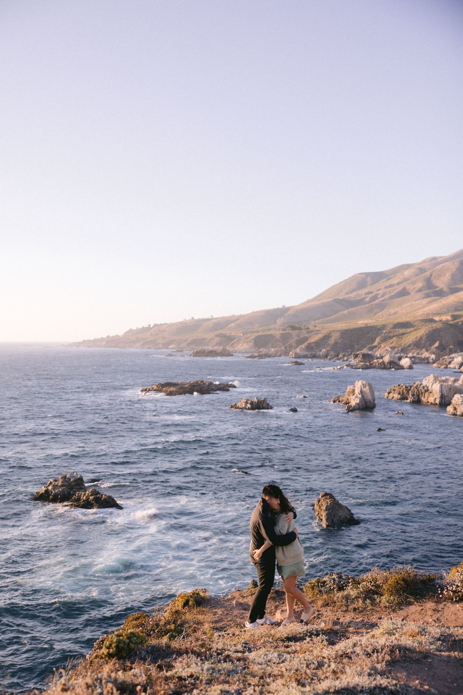 A hiker traverses a scenic coastal trail along the rugged Big Sur coastline in California at golden hour.