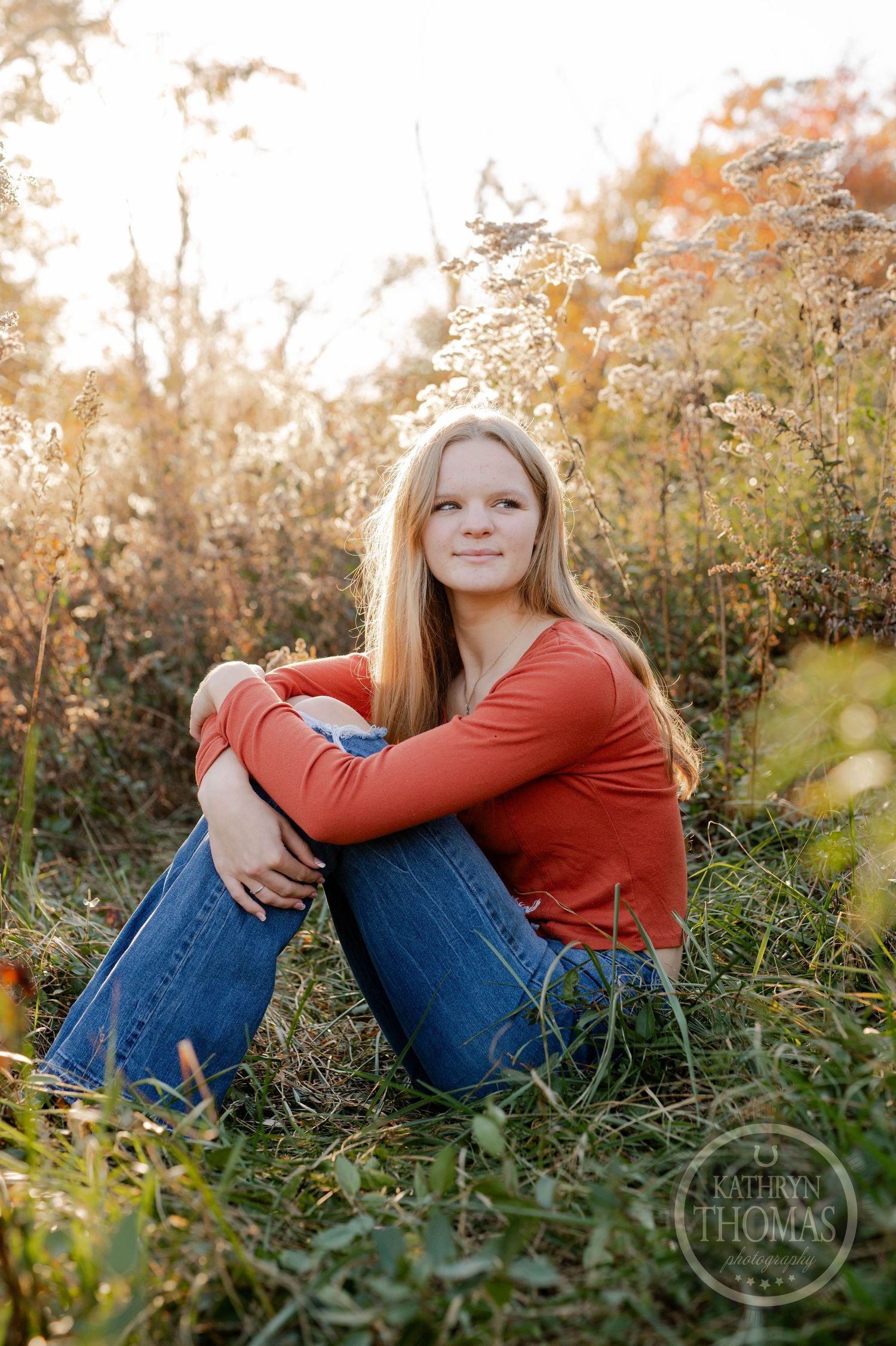 Outdoor autumn portrait with someone in rust-colored top sitting among dried wildflowers.