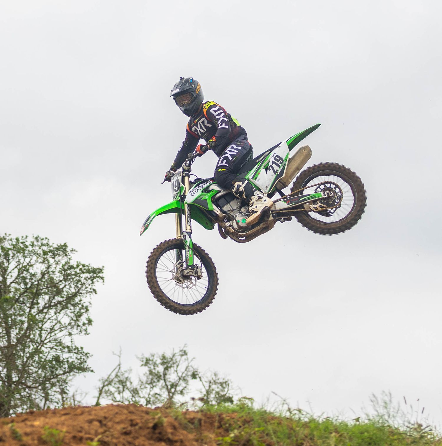 Rider on green Kawasaki motorcycle performing aerial jump on dirt track.