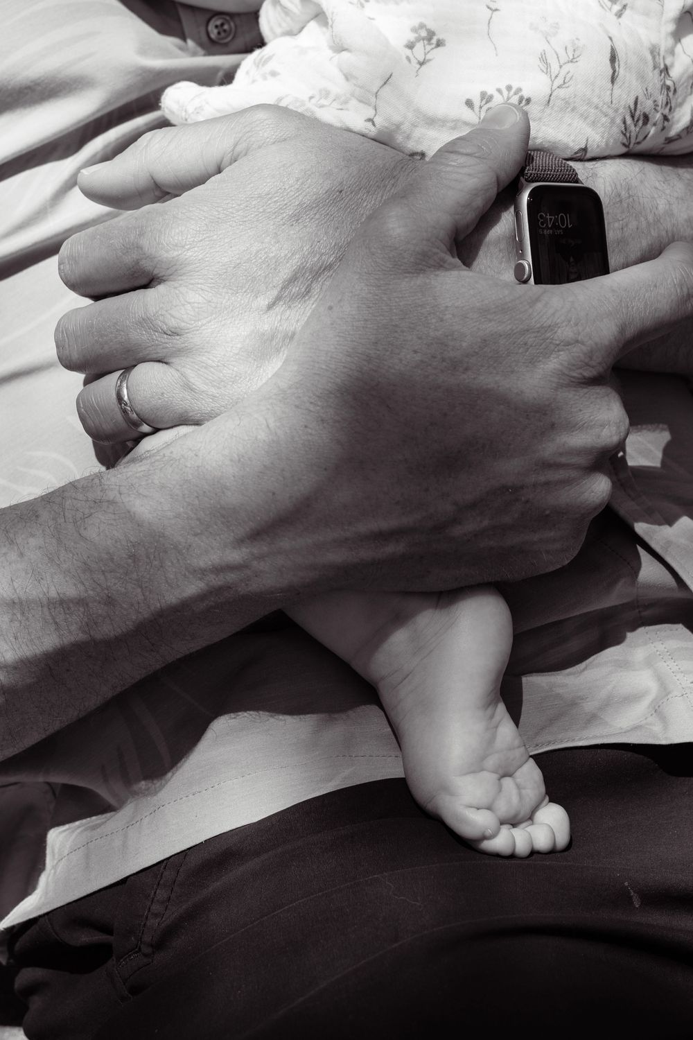 Black and white close-up of dad’s hands holding baby girl, with her tiny foot under his hand in a tender family moment in San Diego.