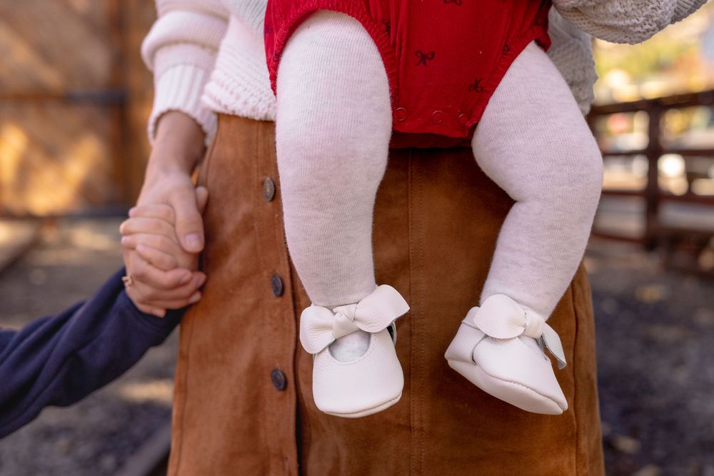 Close-up of baby girl's chubby leggs and feet while being held by the mom, who is also holding her little boy's hands at Old Poway Park.