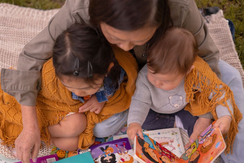 Overhead shot of grandma reading books with two grandkids on her lap in a warm and inviting tone at Old Poway Park.