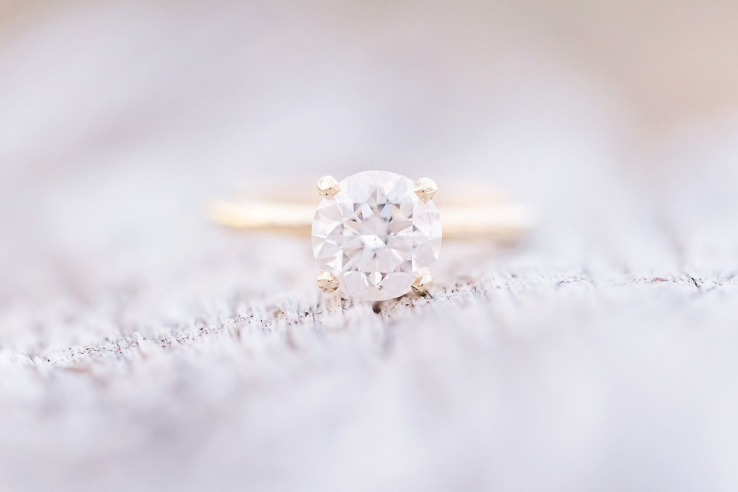 Elegant solitaire diamond engagement ring in rose gold resting on soft white lace fabric with delicate details.