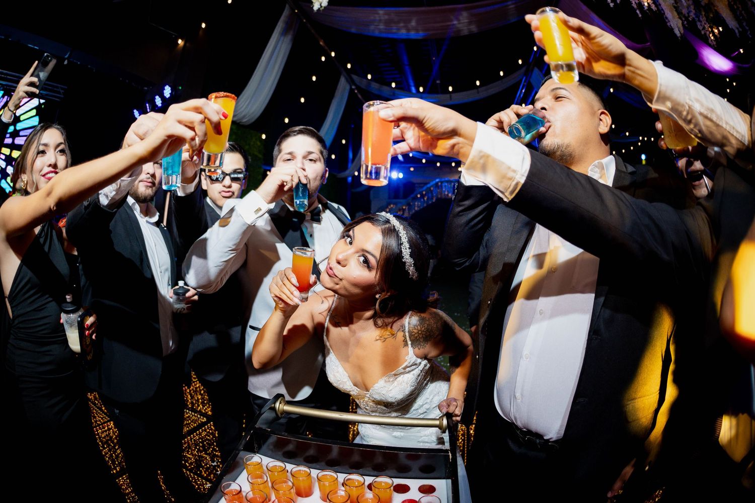 Wedding party guests celebrating and toasting during a lively reception party with dramatic lighting.