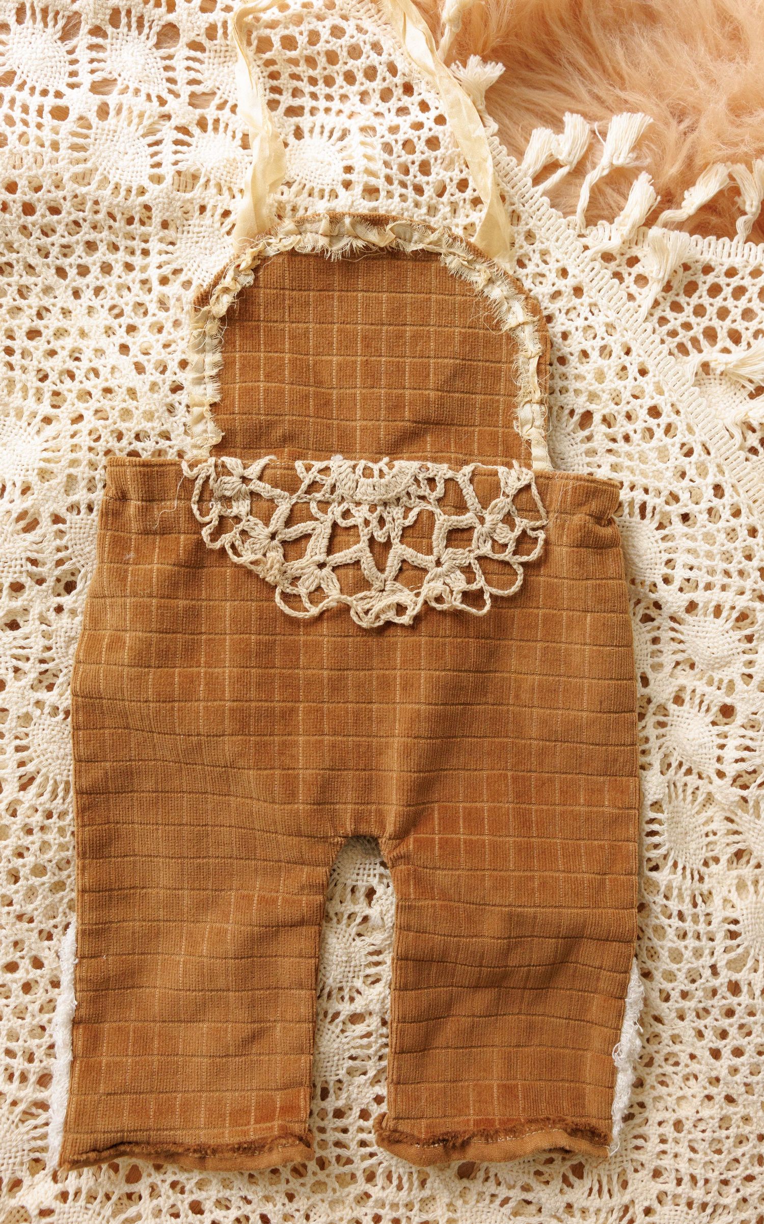 Rustic brown linen baby romper with delicate white lace trim and crochet details displayed on vintage lace background.