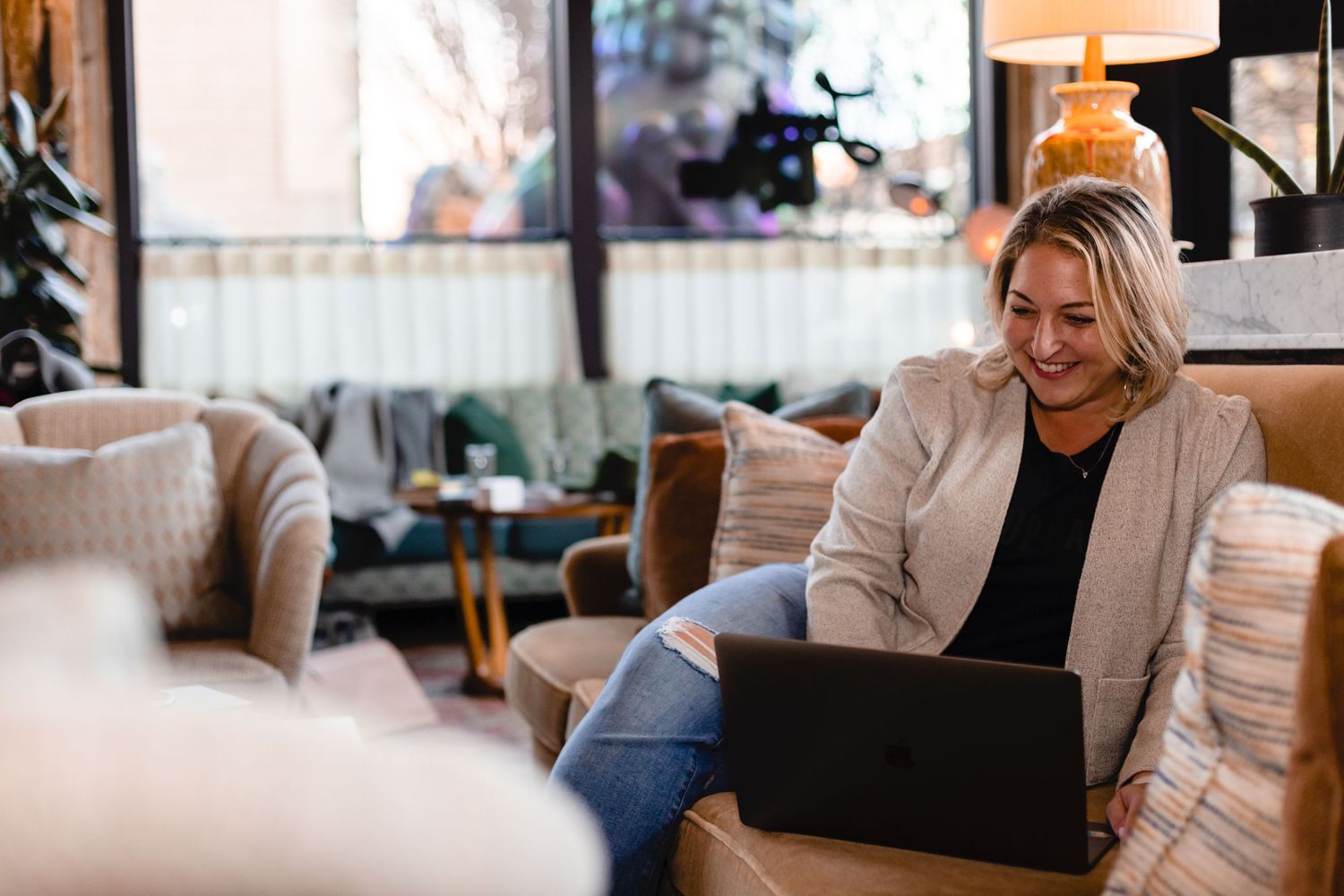 Casual person using laptop while relaxing in cozy chair at home wearing beige cardigan and jeans.