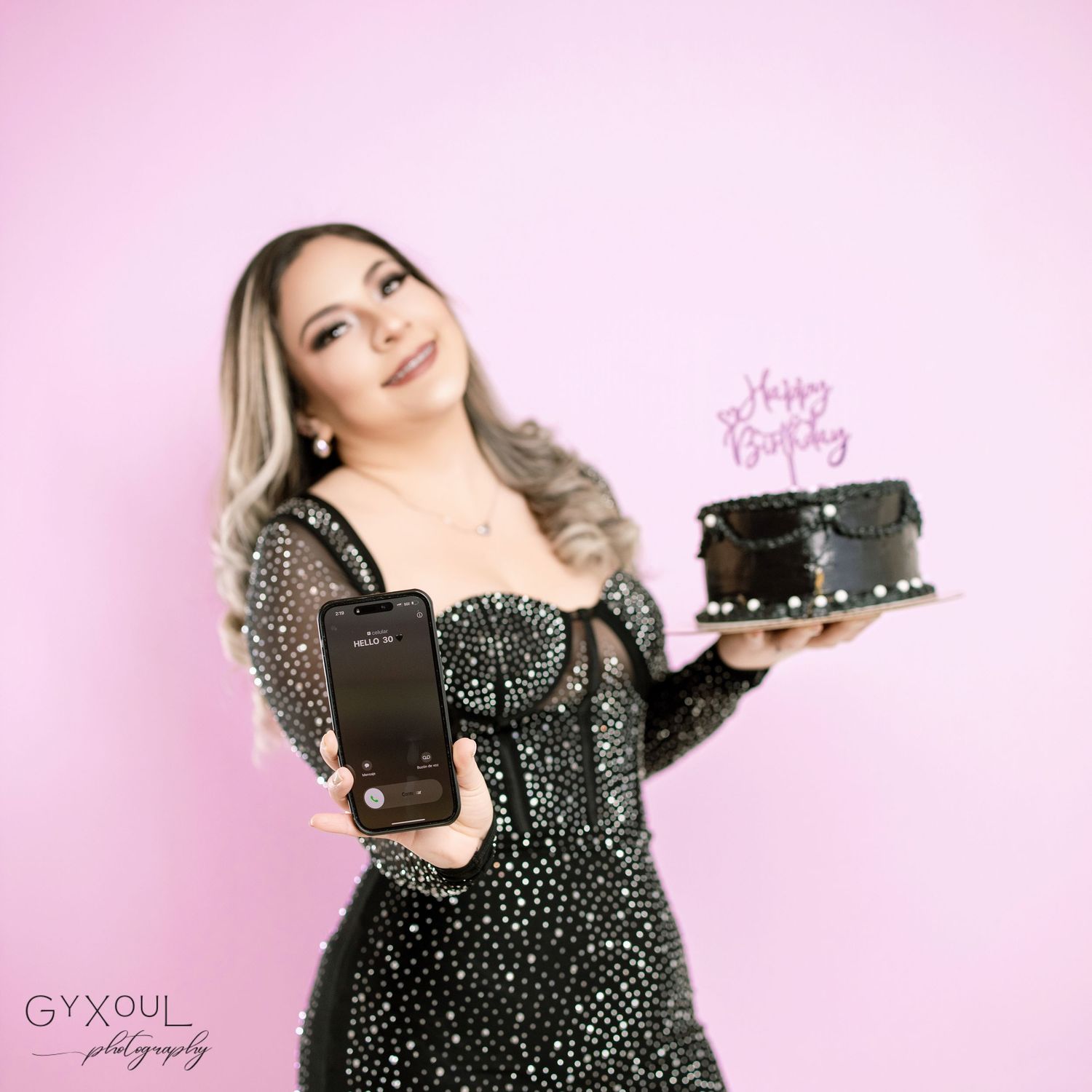 Birthday photo with black smartphone and cake against pink background.