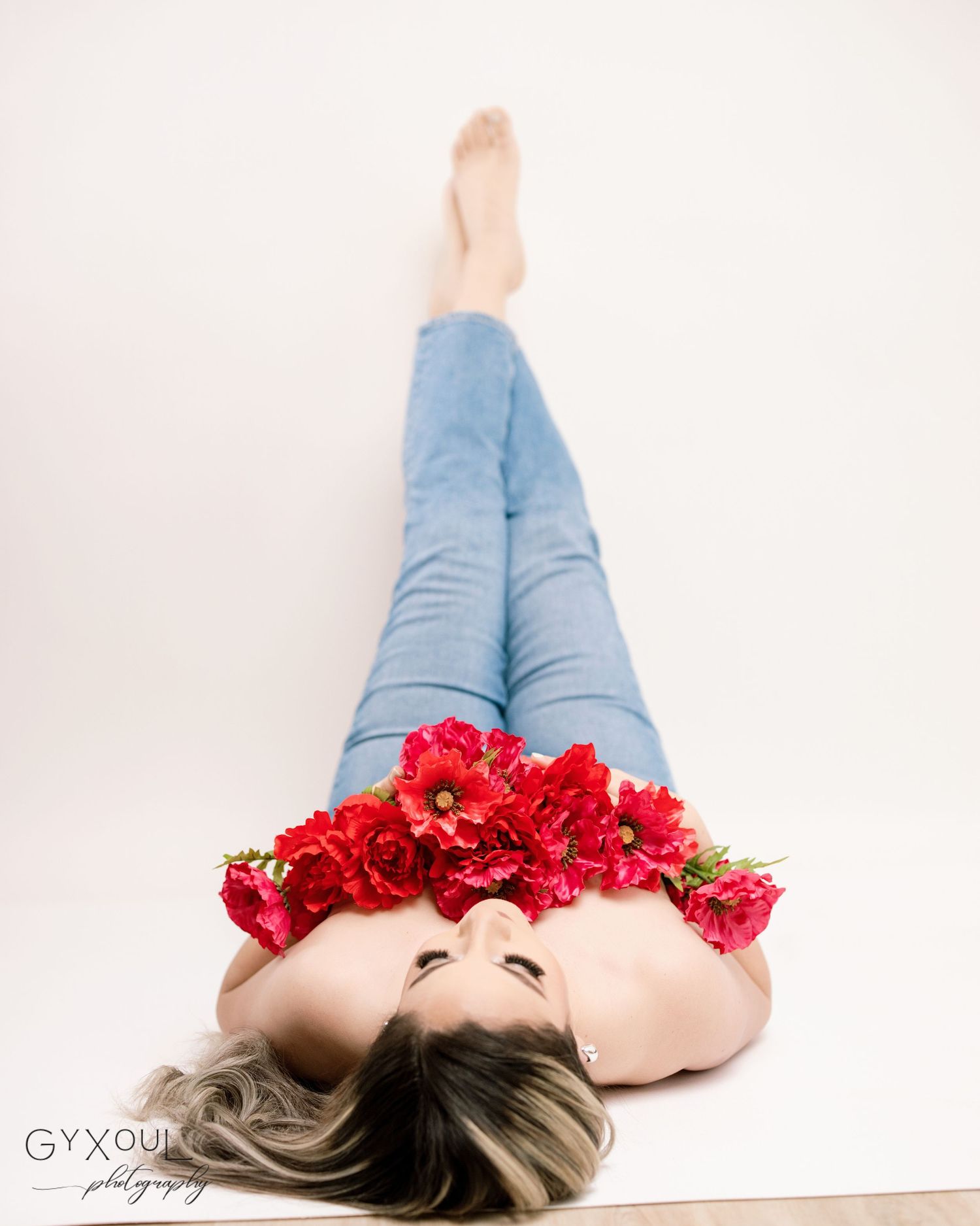 Artistic portrait with red flower crown while lying on white background in denim.
