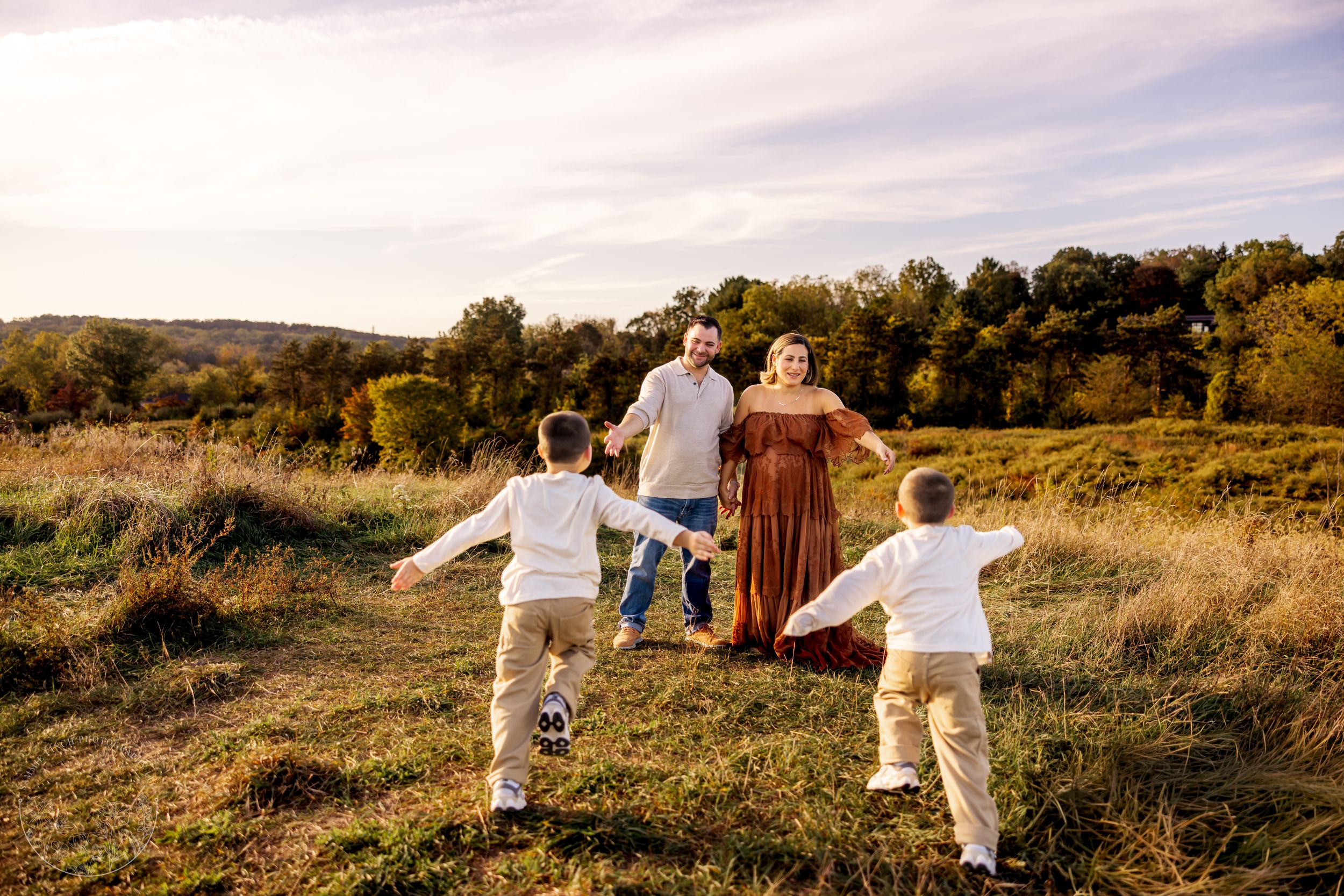 A family holding hands while walking through a golden autumn field at sunset with rolling hills in the background.