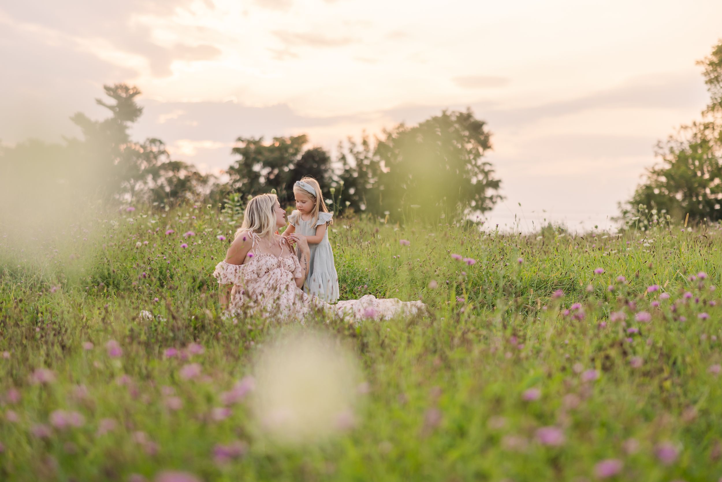 A couple stands together in a lush meadow with wildflowers during sunset creating a romantic outdoor scene.