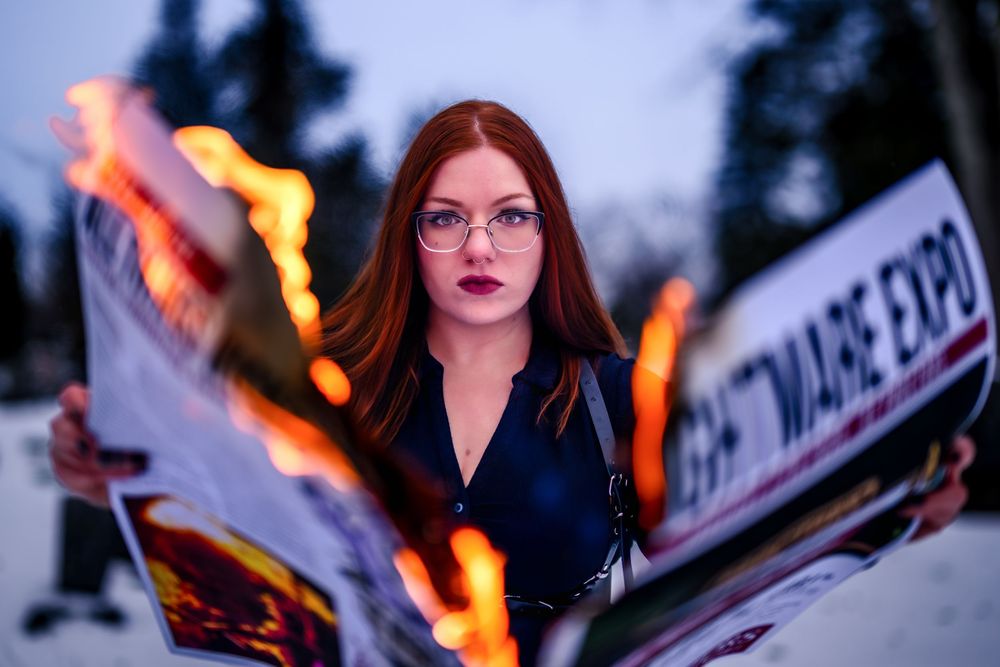 A person holds a burning sparkler against a dark background while wearing glasses and red lipstick.