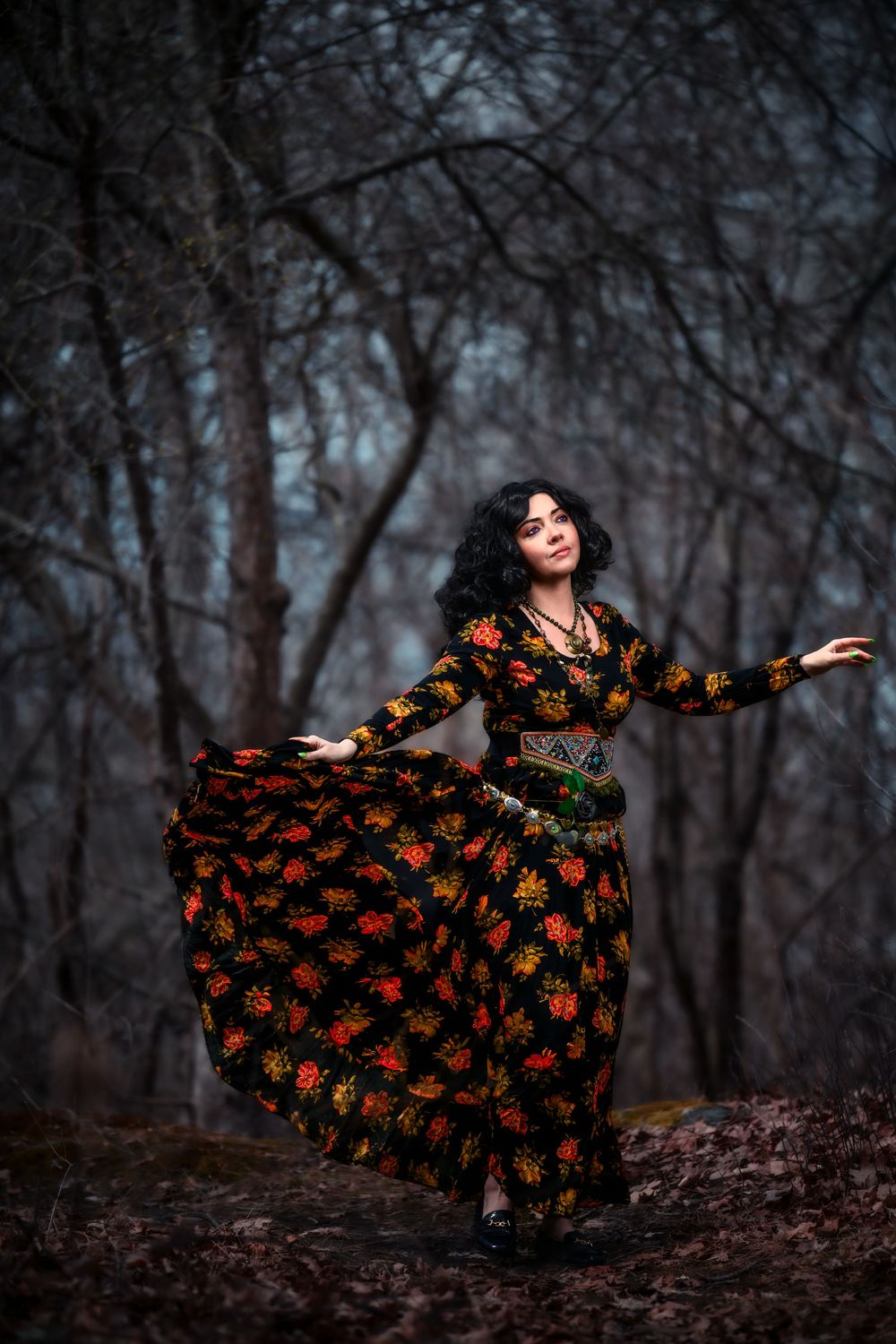 Woman in floral dress dancing in dark forest.