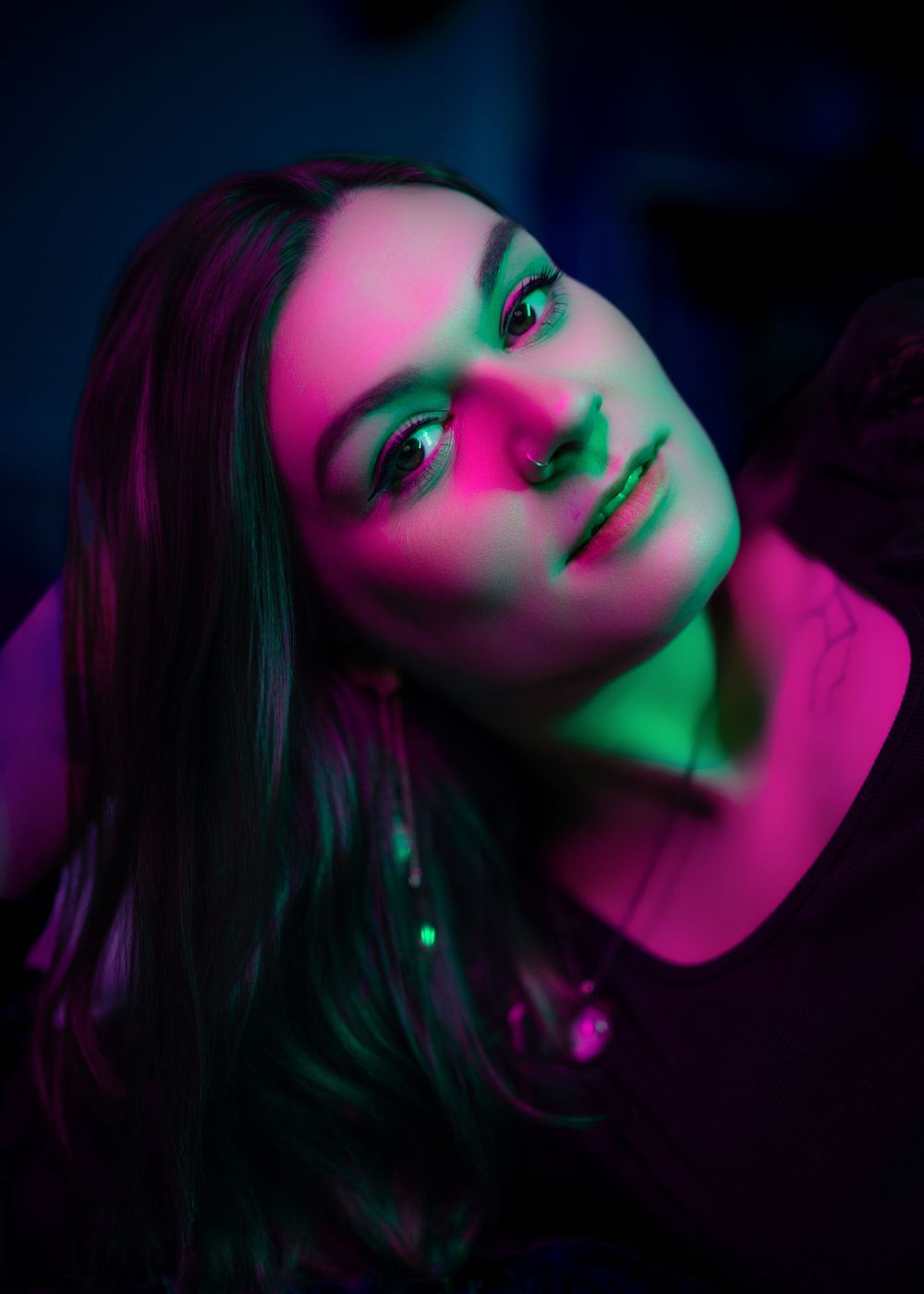 Artistic portrait with dramatic neon pink and green lighting creating moody atmosphere and shadows.