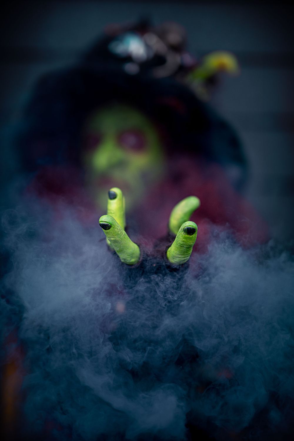 Green witch fingers emerging from dark smoke against a mysterious black background.