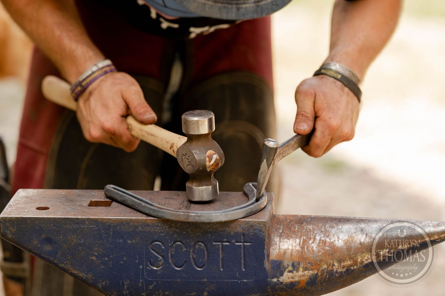 Detailed view of hands using hammering tools on a vintage Scott anvil.