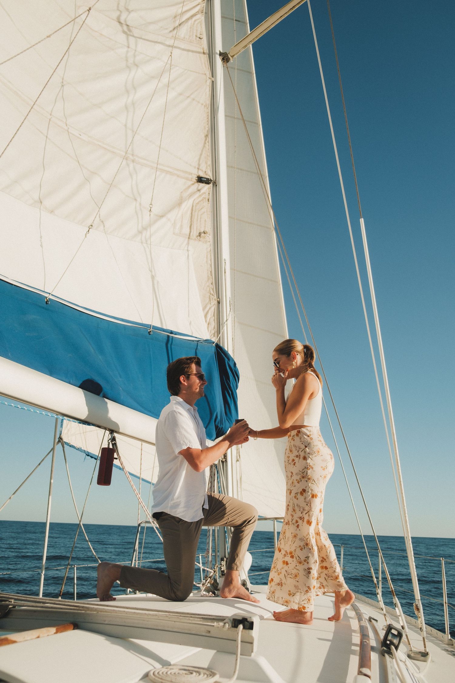 Couple enjoying a romantic moment on a sailboat with white sails against blue ocean.