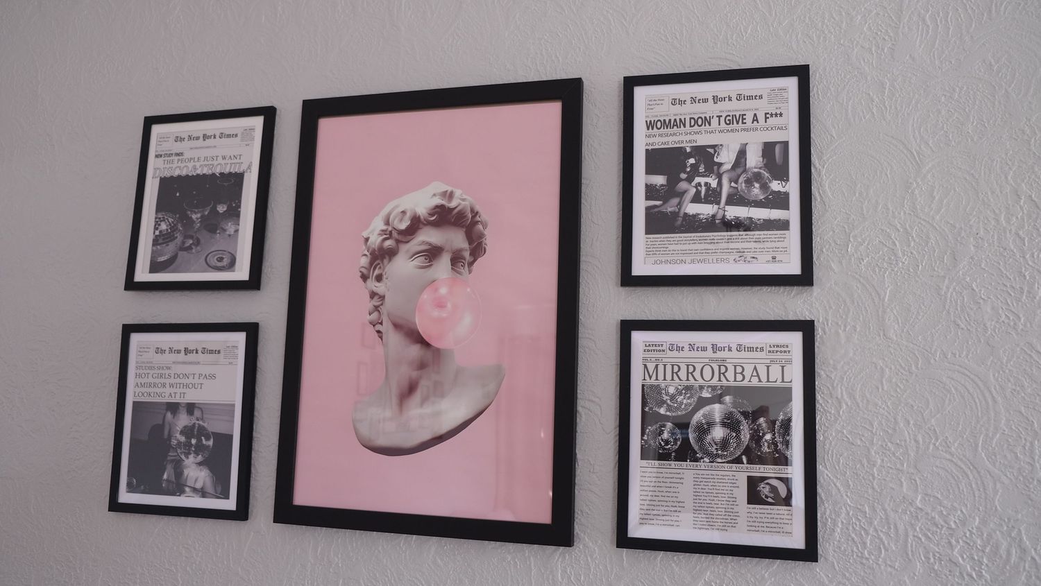 A gallery wall displays a pink-framed classical bust sculpture print surrounded by black and white newspaper clippings.
