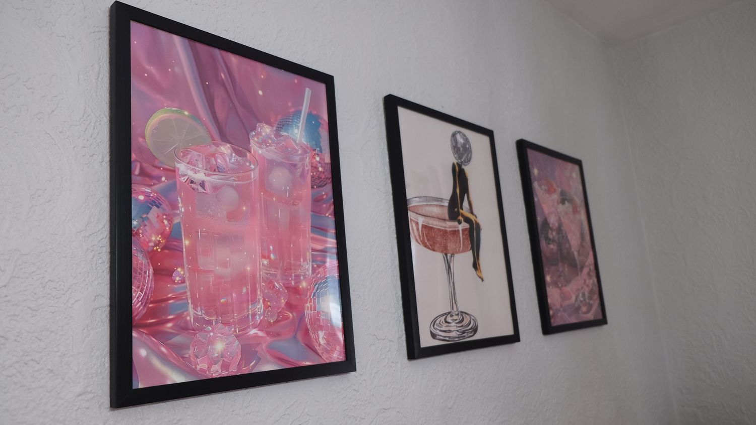 Three framed prints with pink and black tones hang evenly spaced on a white wall.