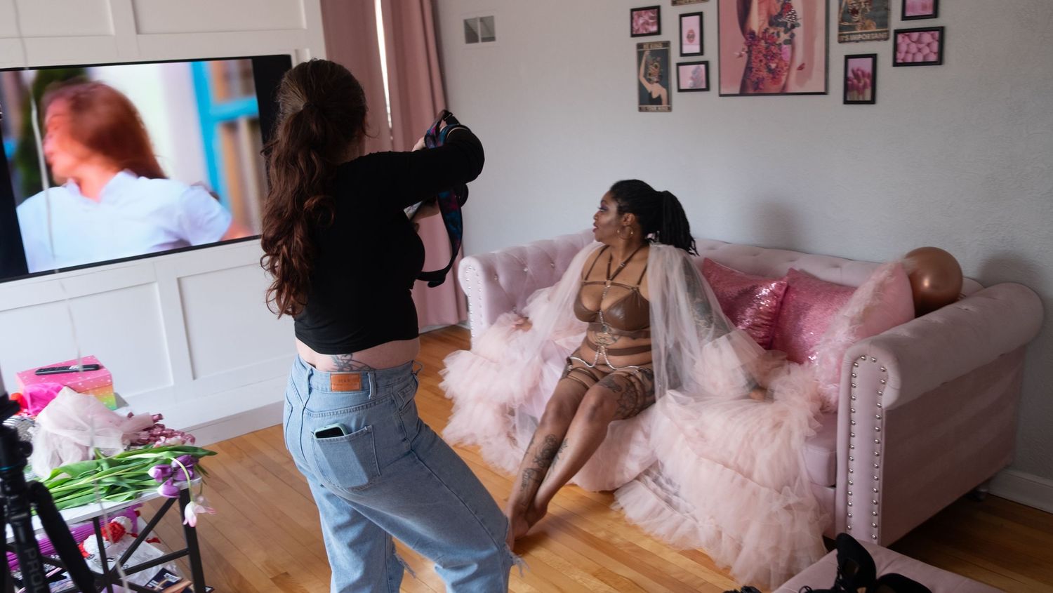 Behind the scenes photo shoot in a bright room with pink couch and framed wall art.