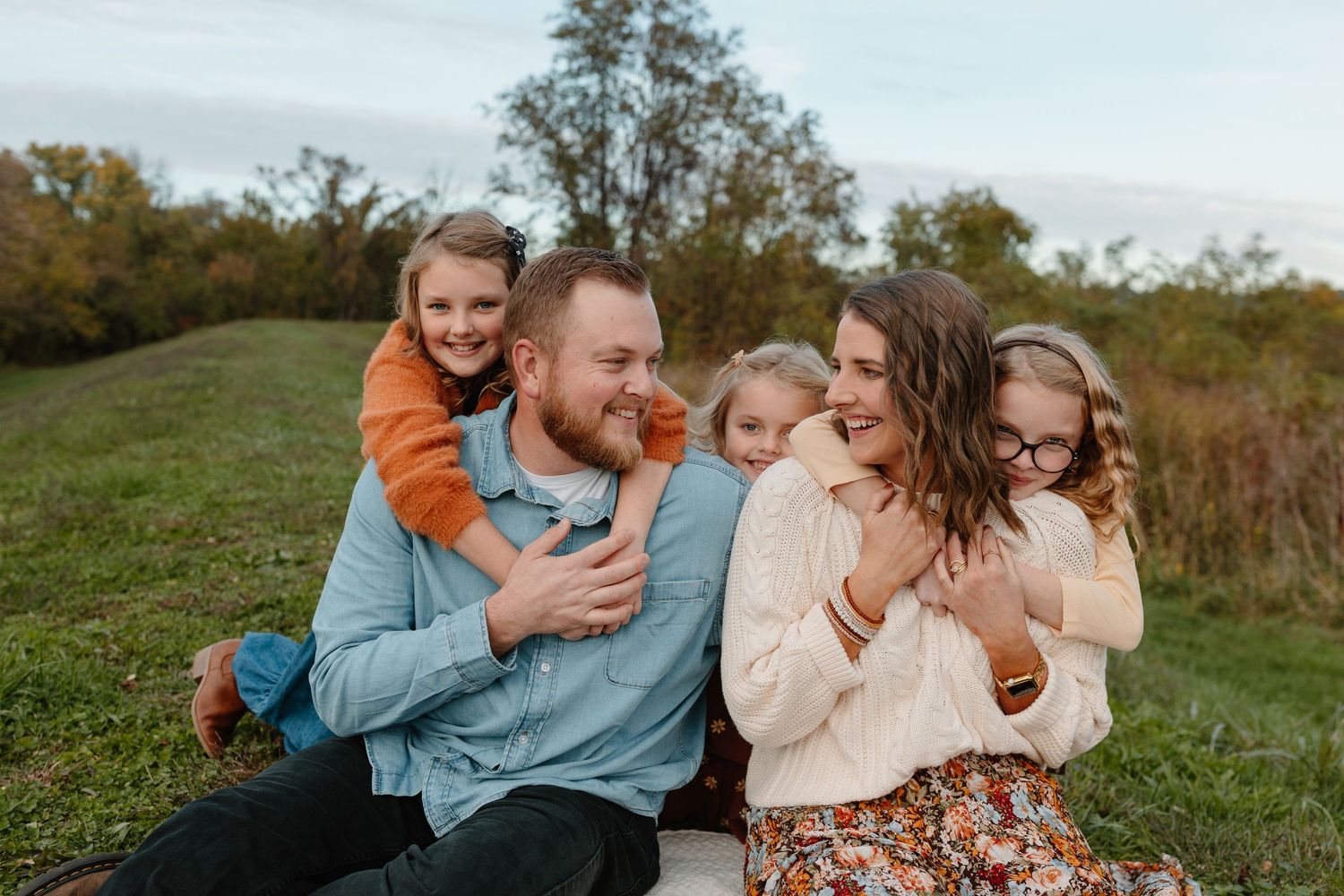 Family sitting together on truck tailgate surrounded by autumn leaves.