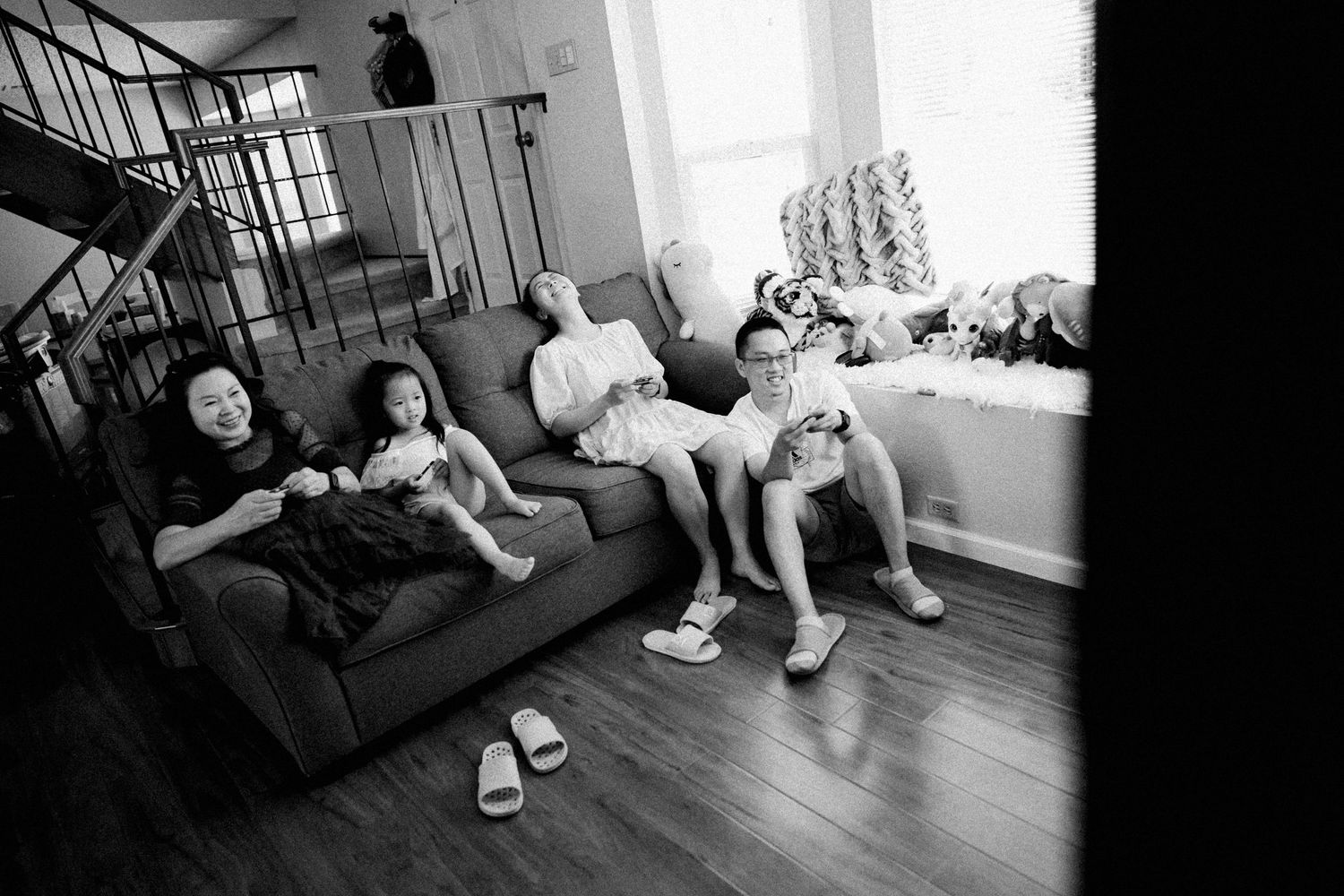 A candid black and white photo showing people relaxing on a couch in a living room with wooden floors.