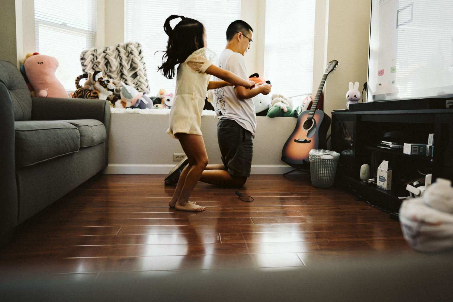 Two people dancing together in a living room with hardwood floors and guitars visible in the background.