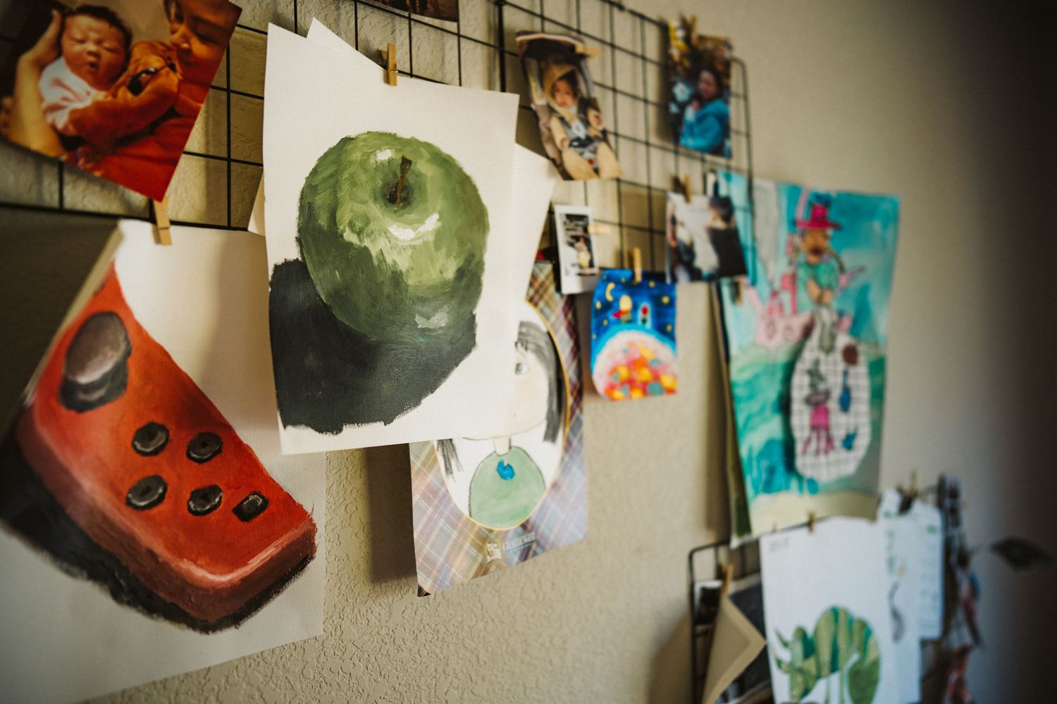 Artwork and drawings displayed on a wall include a red calculator, green apple, and various other colorful pieces.