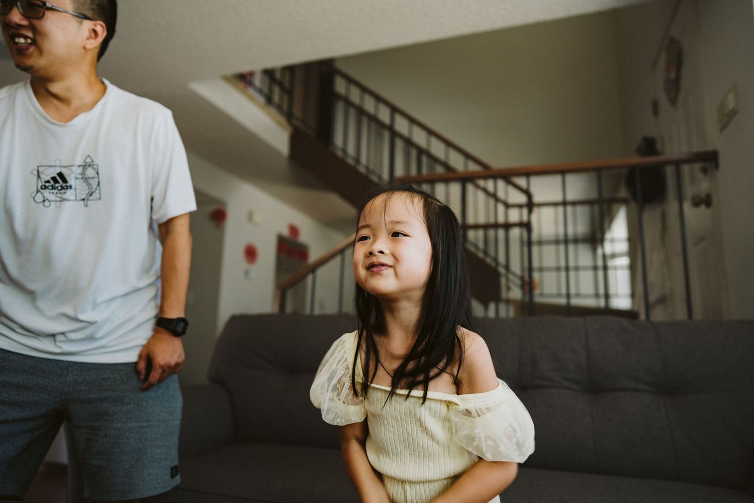 A young child laughs joyfully while sitting on a grey couch in a home setting.