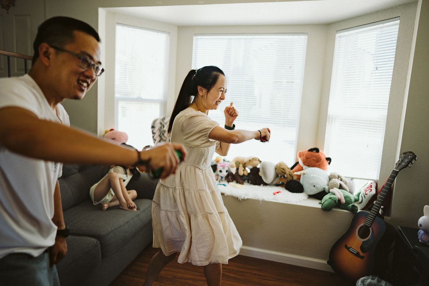 Two people dancing energetically together in a bright living room with a bay window.