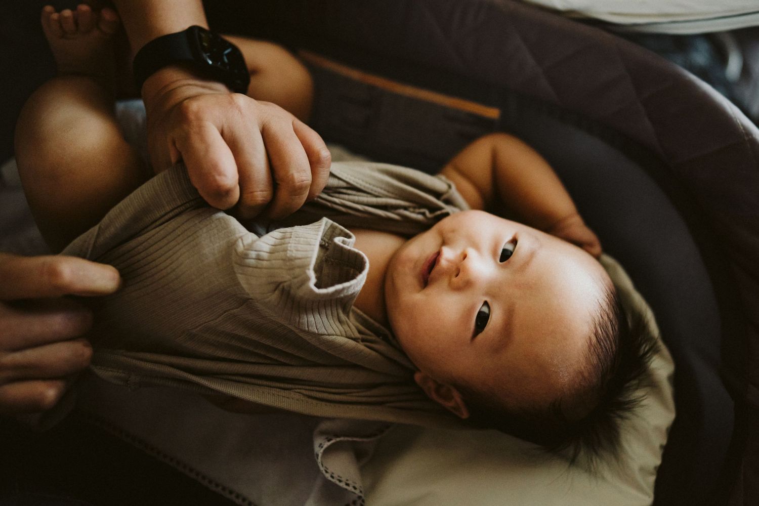 A toddler lying down while wearing a gray shirt and smiling at the camera.