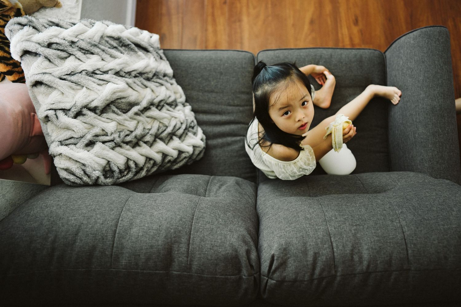 A small child relaxes on a gray couch with a decorative textured pillow.
