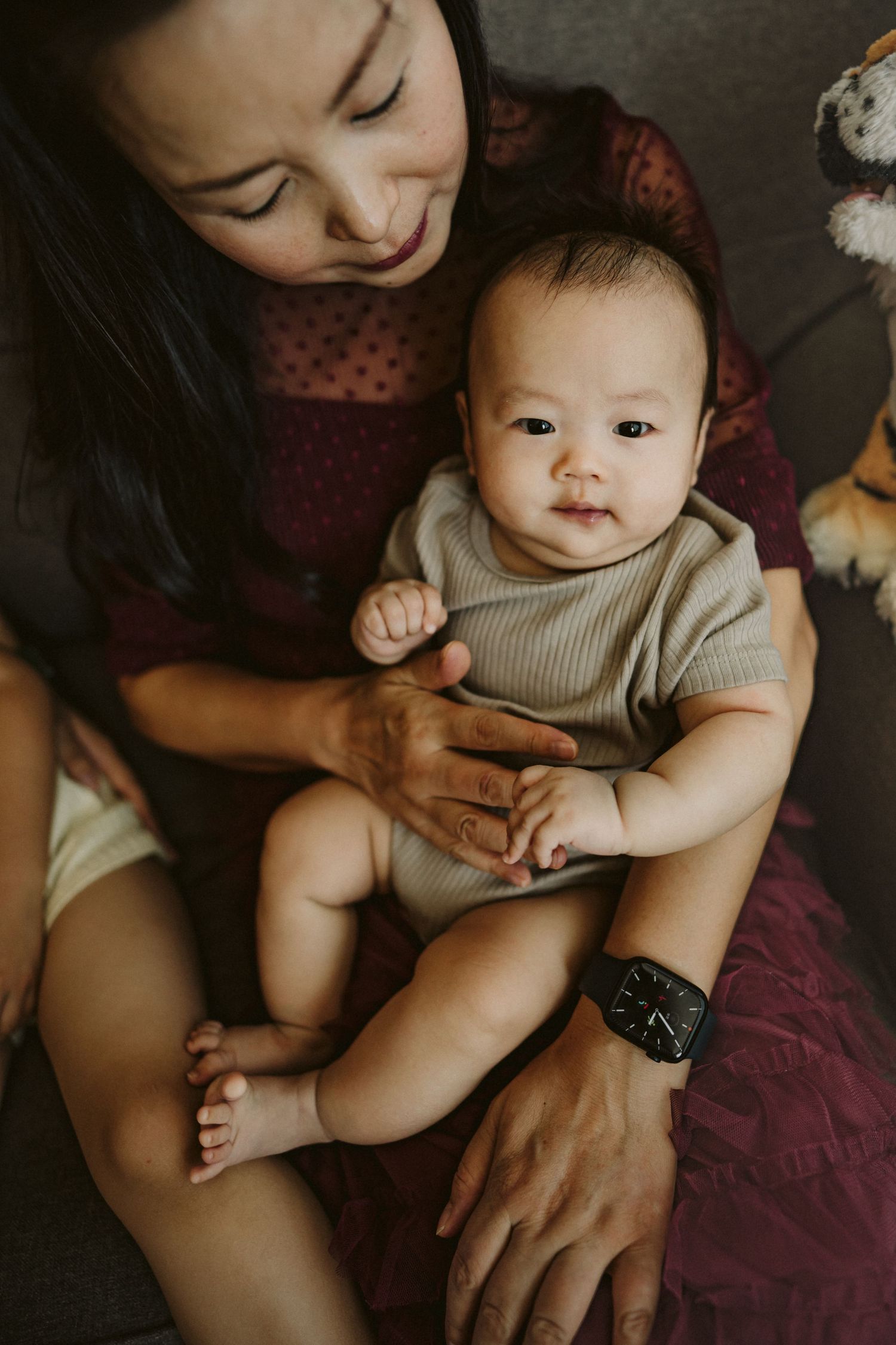 A warm moment captured between parent and baby in a burgundy-toned setting with soft lighting.