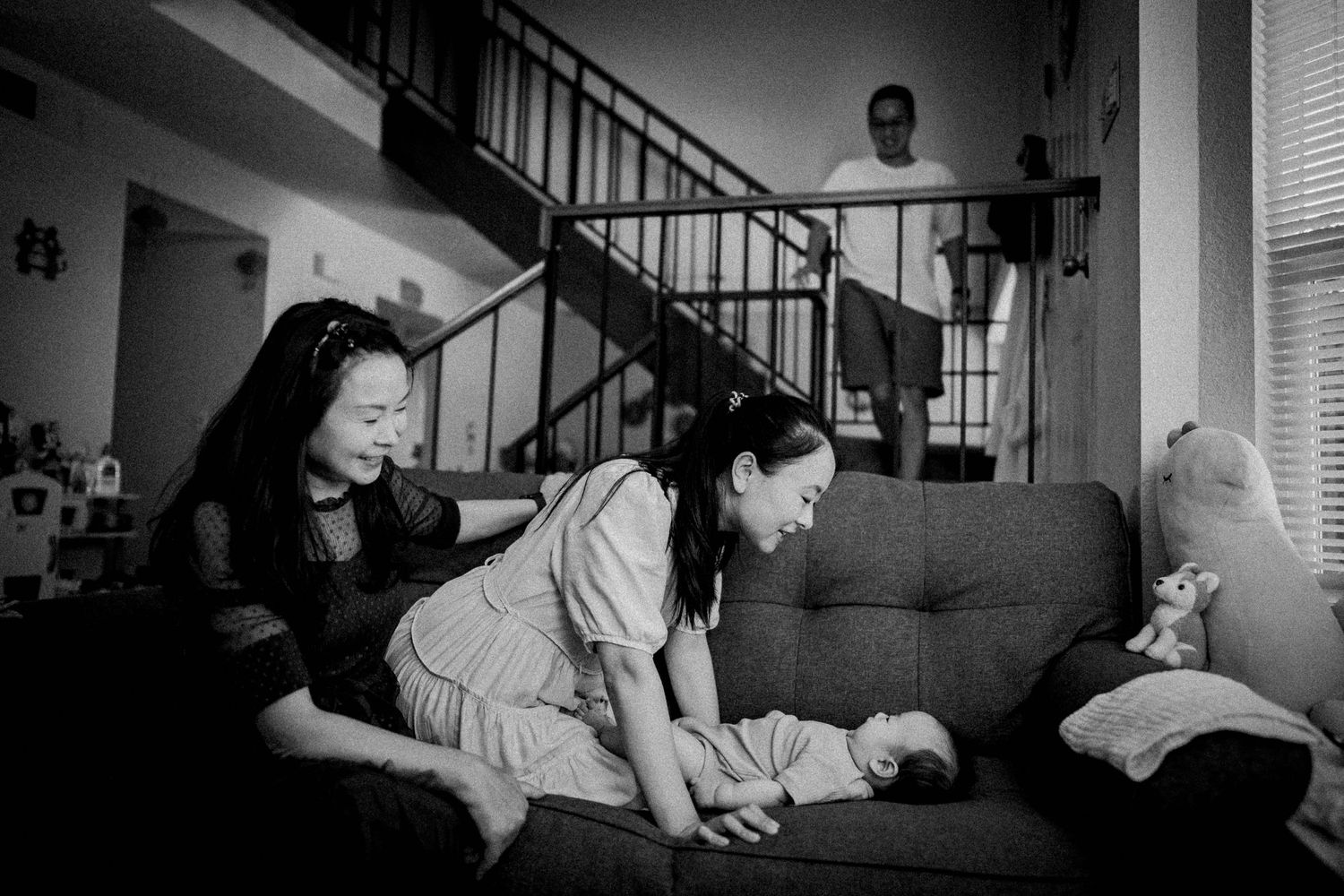 Black and white photograph of people gathered in a living room with stairs visible in the background.