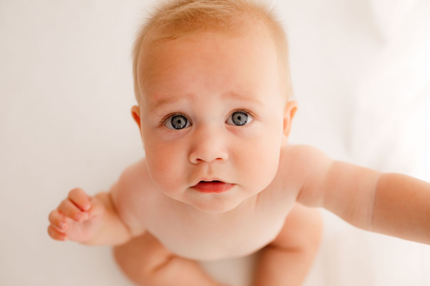 Baby in white clothing lying on white backdrop during professional photo session.