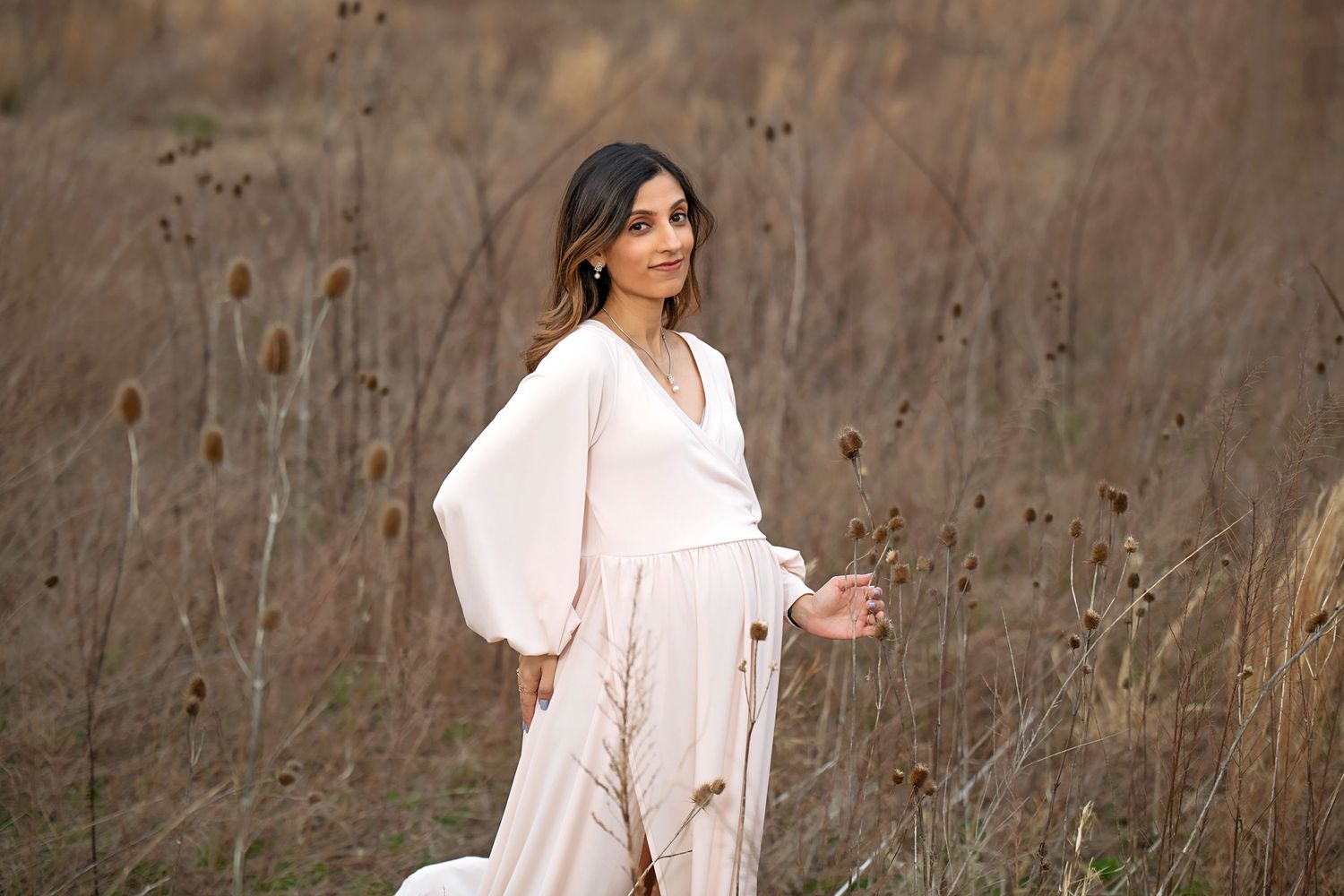 Outdoor portrait in flowing cream dress against autumn field backdrop.