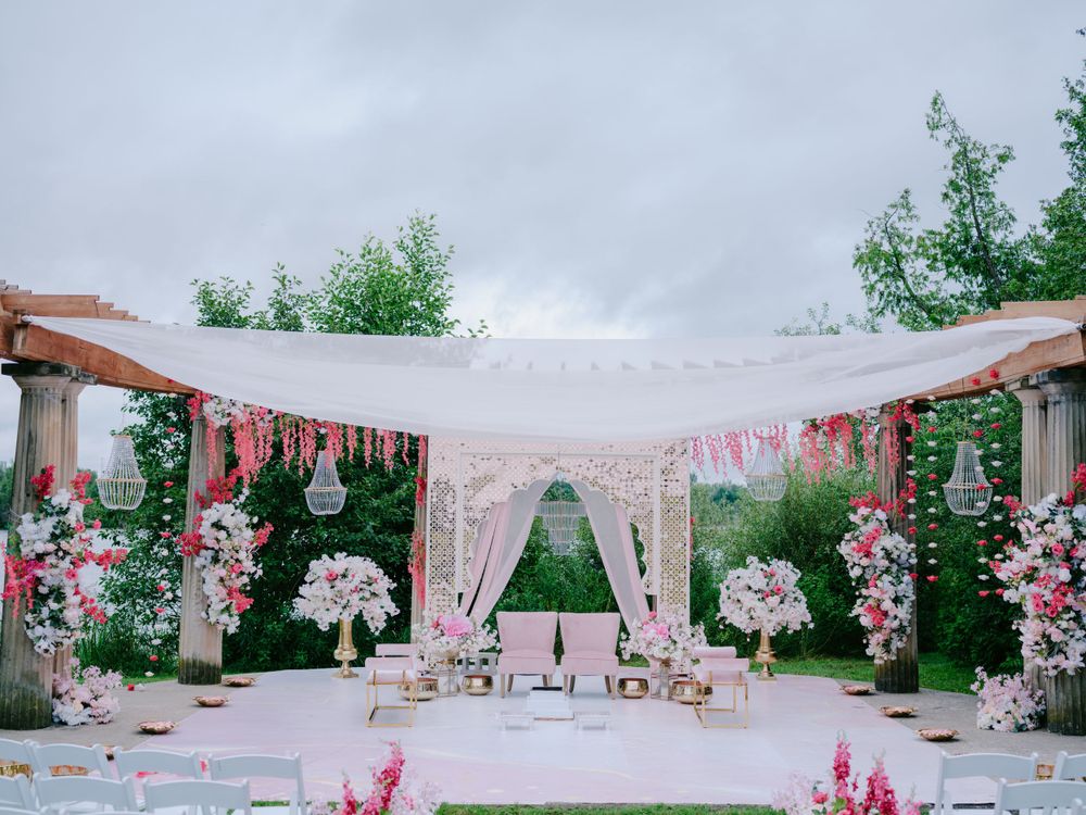 Elegant outdoor wedding venue decorated in pink and white with floral arrangements, drapes and a romantic garden setting.