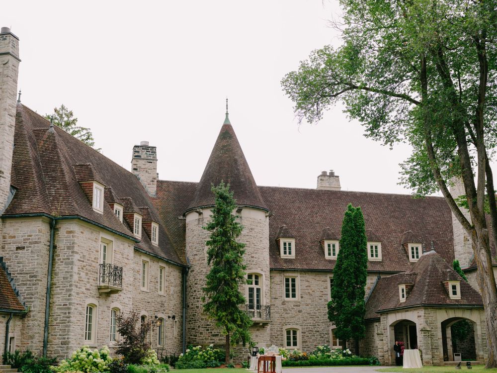 Historic French chateau with stone walls, steep brown roofs, tall cypress trees and multiple chimneys in a tranquil setting.