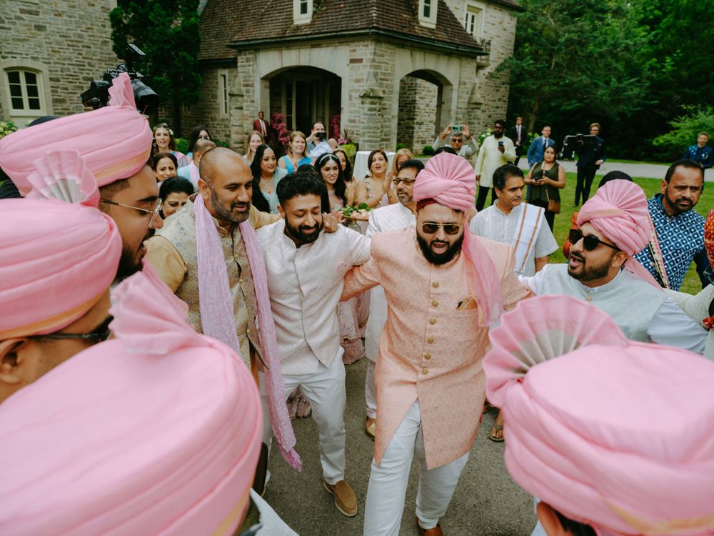 Wedding celebration with guests dressed in pink and white gathered outside a stone mansion.