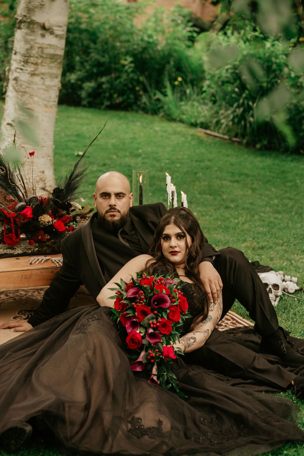 A dramatic gothic photoshoot features a couple in black with red roses and outdoor decor.