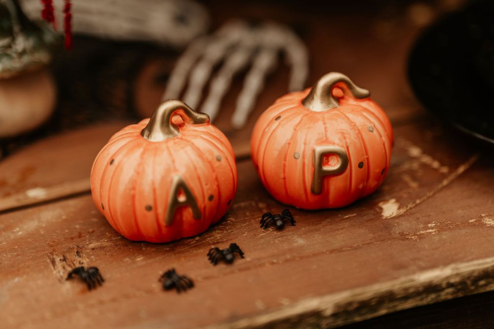 Two decorative ceramic pumpkins with letters A and P painted on them sit beside small black objects on a wooden surface.
