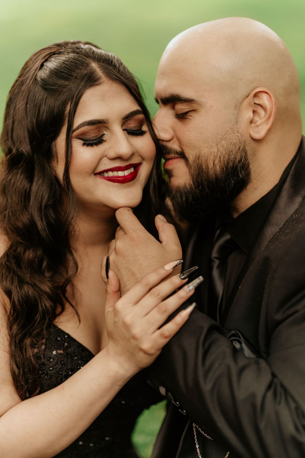 Romantic couple shares an intimate moment outdoors with woman in black dress and man in dark shirt.