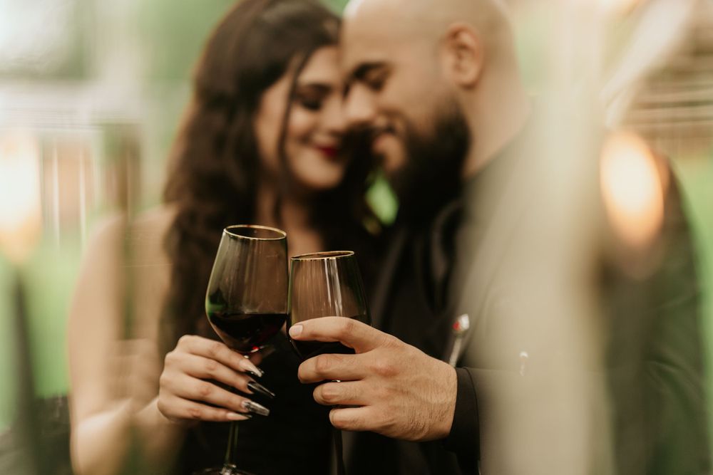 A couple holds red wine glasses while sharing an intimate moment in soft, romantic lighting.