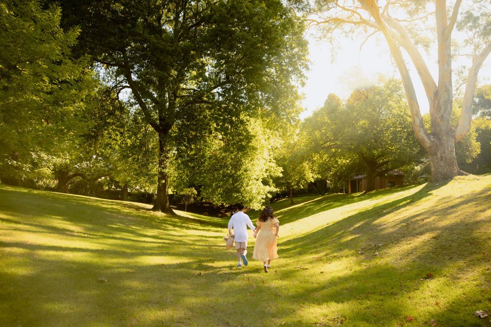 Two figures walking hand in hand through a sun-drenched grassy hill.