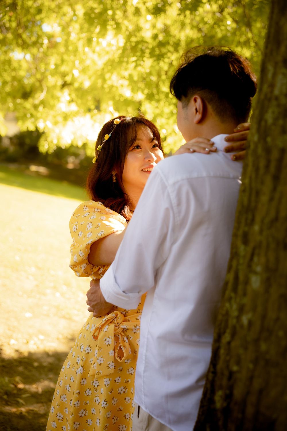 Two people sharing an intimate moment under golden sunlit trees.