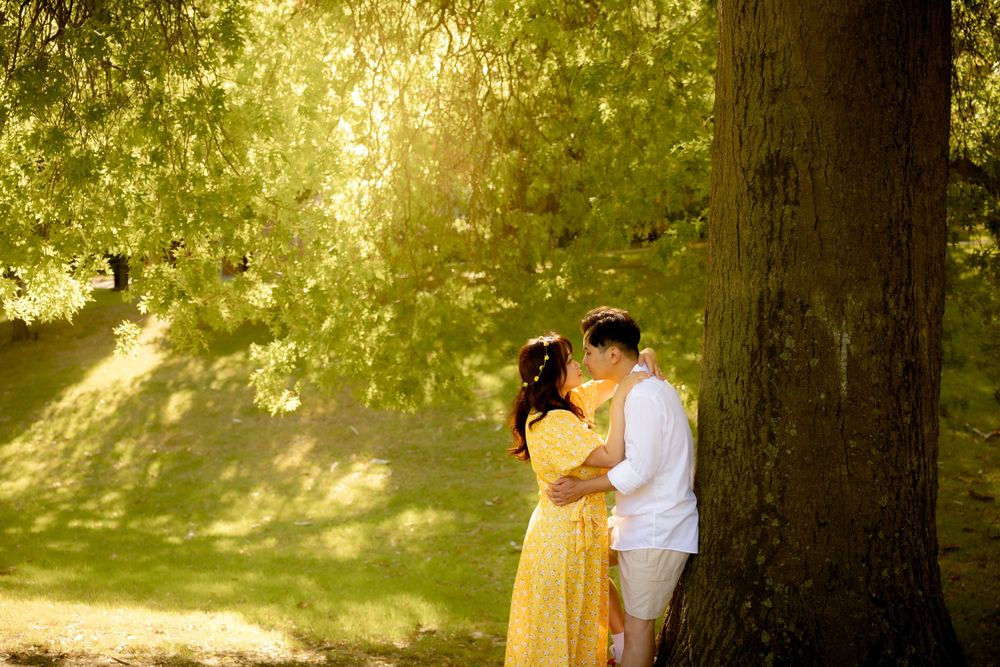 A romantic scene unfolds as a couple shares an intimate moment against a large tree in dappled sunlight.